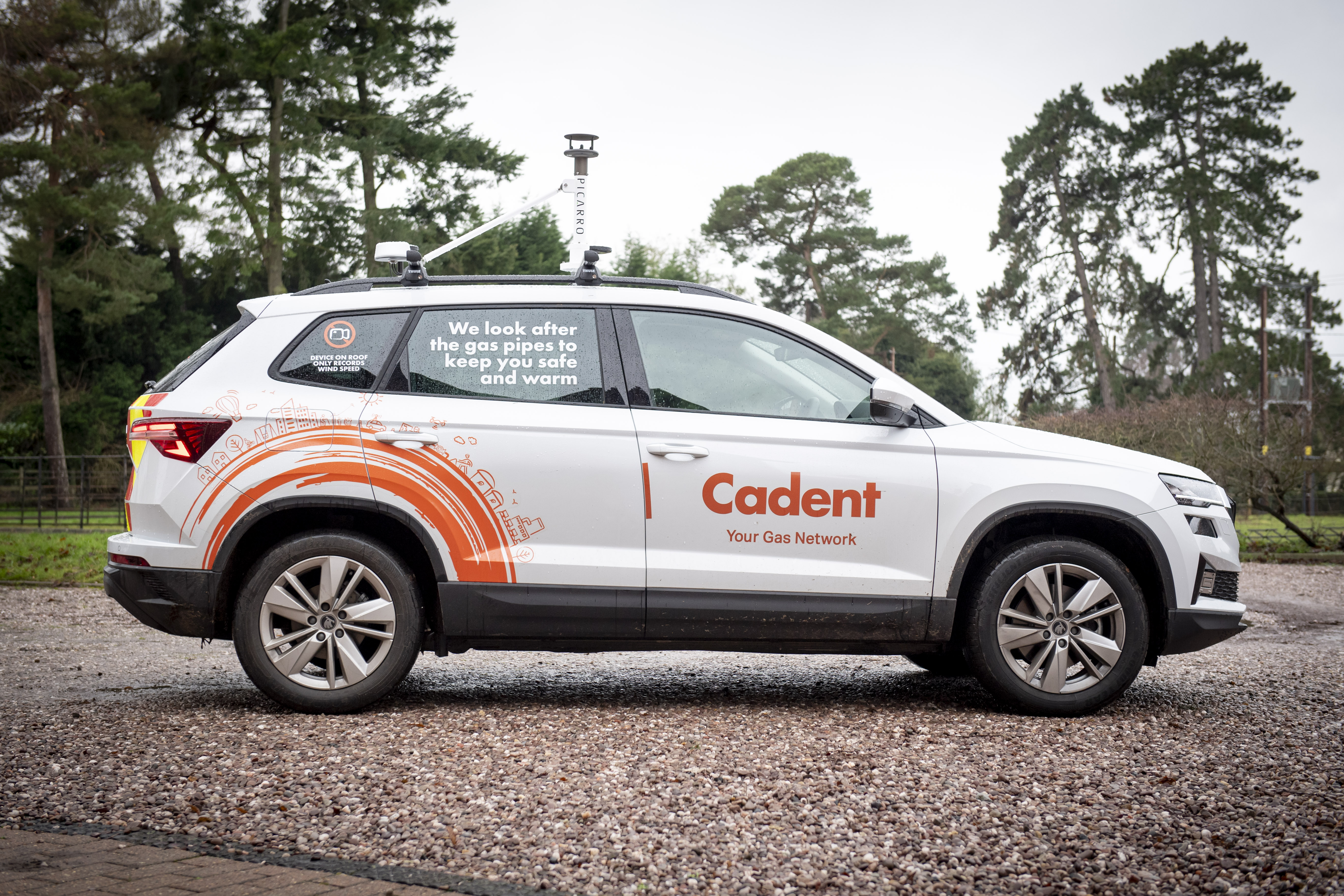 White Cadent utility vehicle parked on a gravel drive, featuring orange branding and a gas safety message, surrounded by trees.