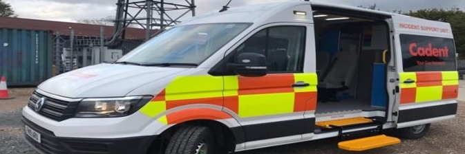 White incident support van with red and yellow reflective stripes is parked with its side door open, displaying a yellow step. Overcast sky in the background.