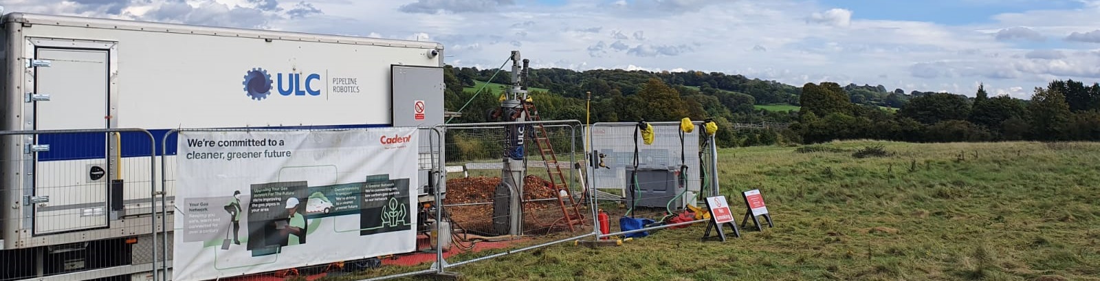 A mobile science lab set up in a grassy field, with ULC branding. The banner reads 'We're committed to a cleaner, greener future,' conveying innovation and environmental focus.