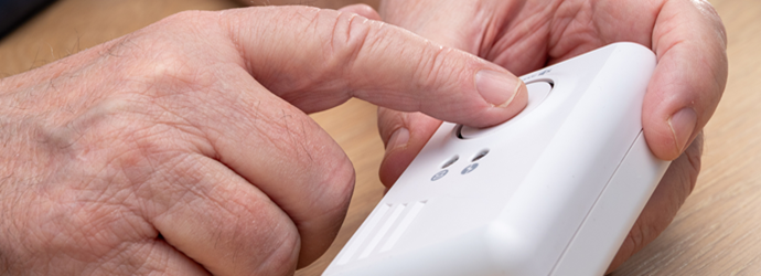 Close-up of hands pressing a button on a white medical alert device.