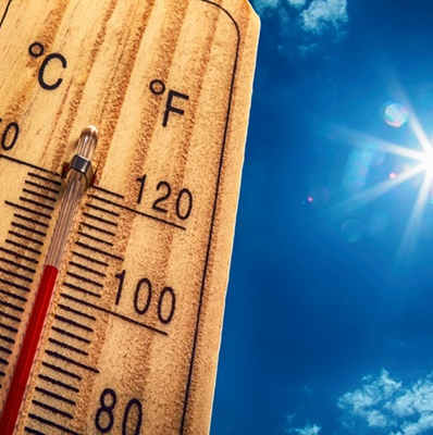 Wooden thermometer showing high temperature under bright sun in a clear blue sky.