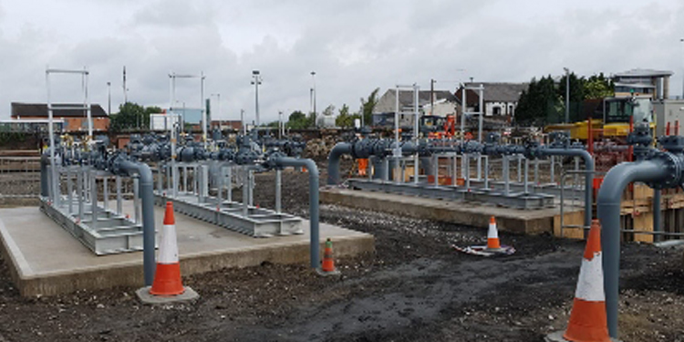 Industrial gas installation with multiple metal pipes and valves mounted on concrete platforms, surrounded by traffic cones at a construction site.