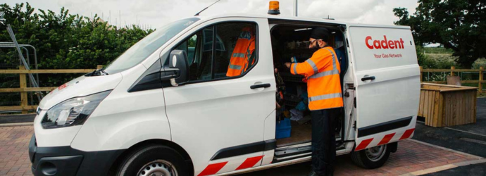White Cadent service van parked outdoors with the side door open, showing a worker in a high‑visibility orange jacket handling equipment inside the vehicle; the Cadent logo and ‘Your Gas Network’ text are visible on the van’s side.